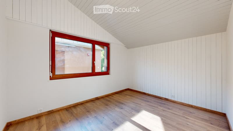 Empty room with white paneled walls, wooden flooring, and a large window with red frame. No furniture or equipment present.