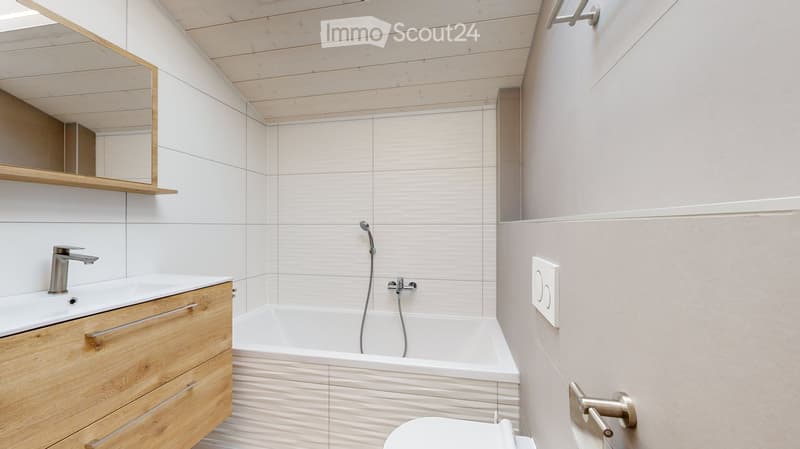 Modern bathroom with white tiles, wooden vanity, sink, bathtub, and mirror.