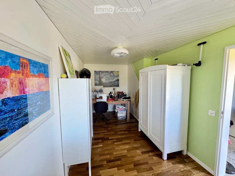A well-lit room with wooden flooring, white cabinets, a desk with a chair, and several framed pictures on the walls.