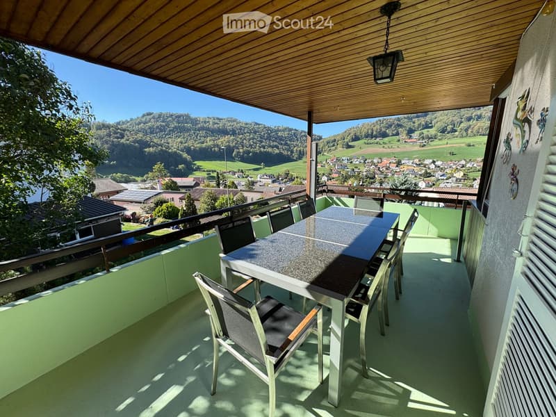 Balcony with a table and chairs, overlooking a scenic valley and town.
