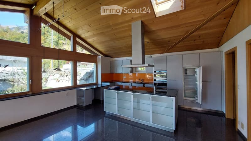 Modern kitchen with white cabinets, stainless steel appliances, and a central island. Large windows offer a scenic mountain view.