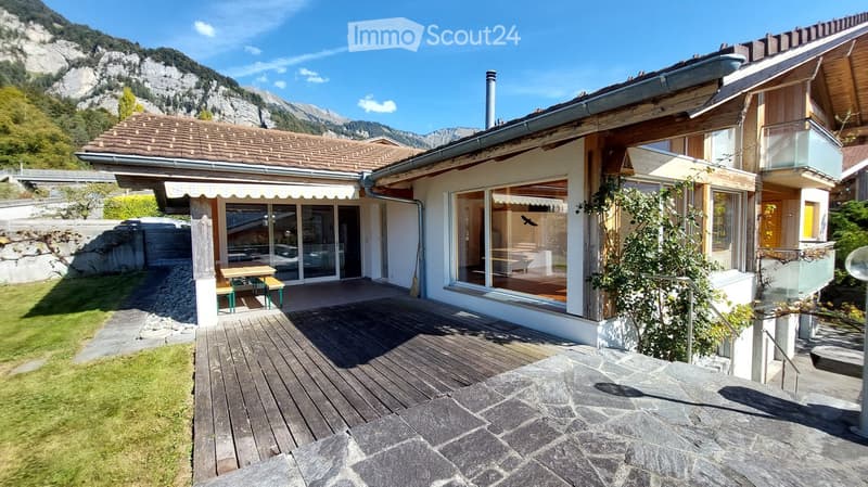 A modern two-story house with a wooden deck, large windows, and a scenic mountain view in the background.