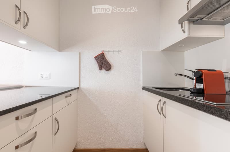Modern kitchen with white cabinets, stainless steel handles, black granite countertops, and a coffee maker on the counter.