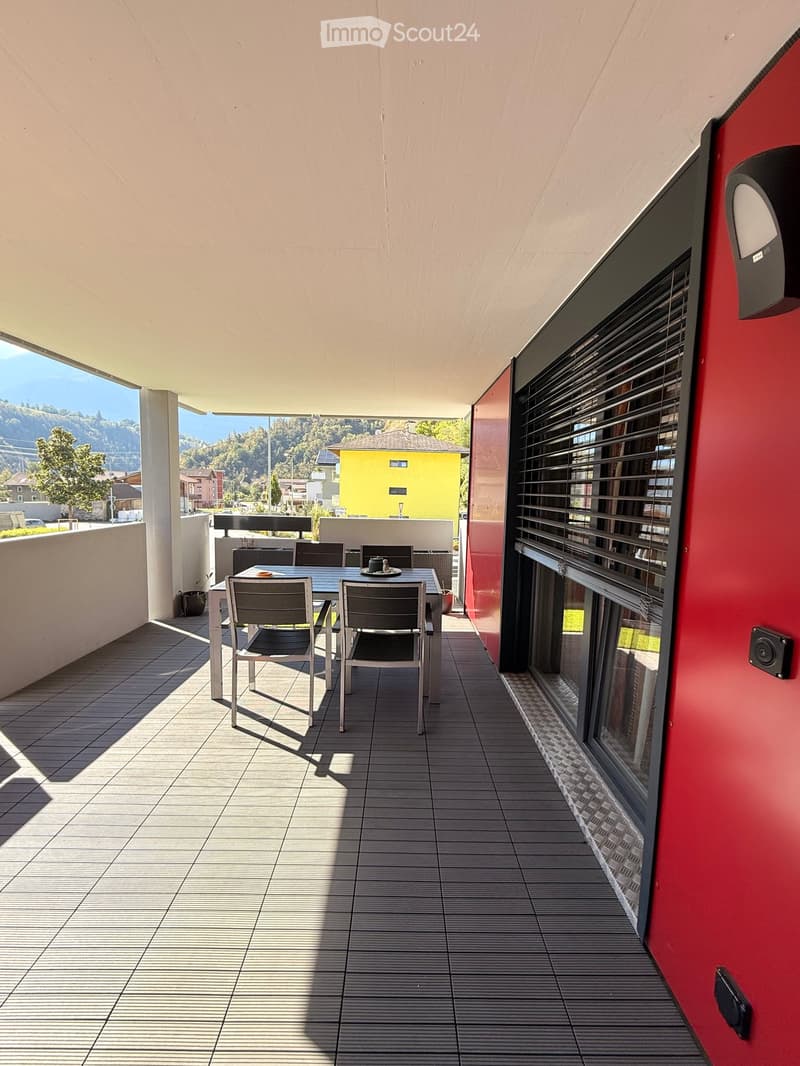 Balcony with tiled floor, modern furniture including a table and chairs, large windows with blinds, and a scenic view of the surrounding area.