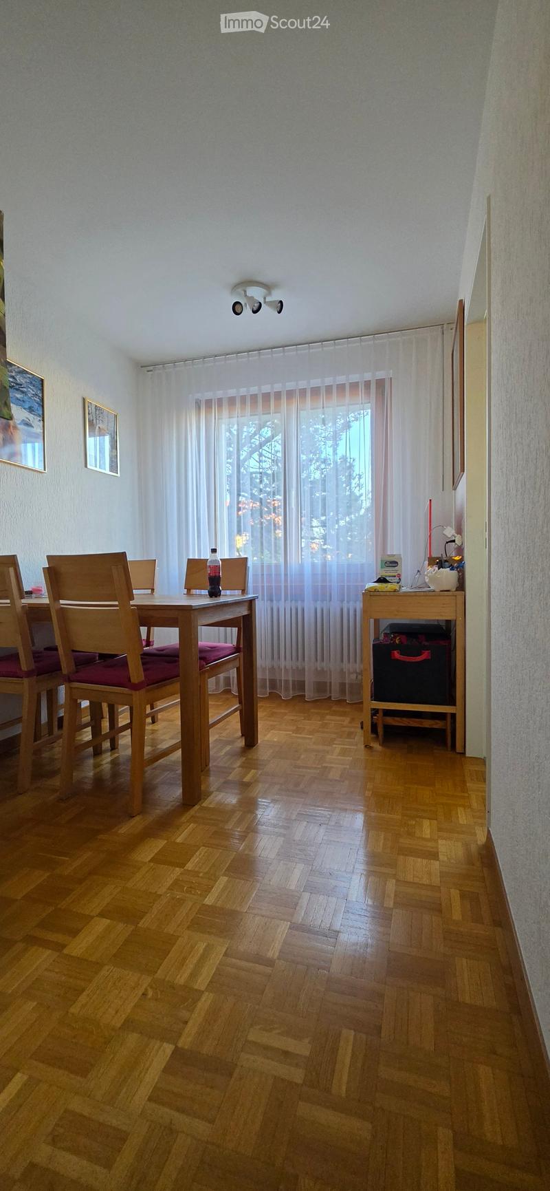Dining room with wooden floor, dining table, chairs, and a small cabinet with items on top.