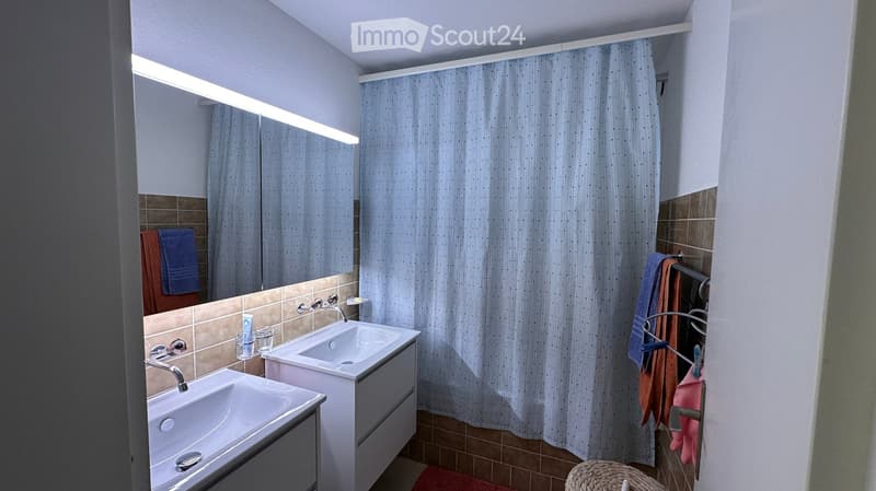 Modern bathroom with two sinks, a large mirror, a shower curtain, and towels on a rack.
