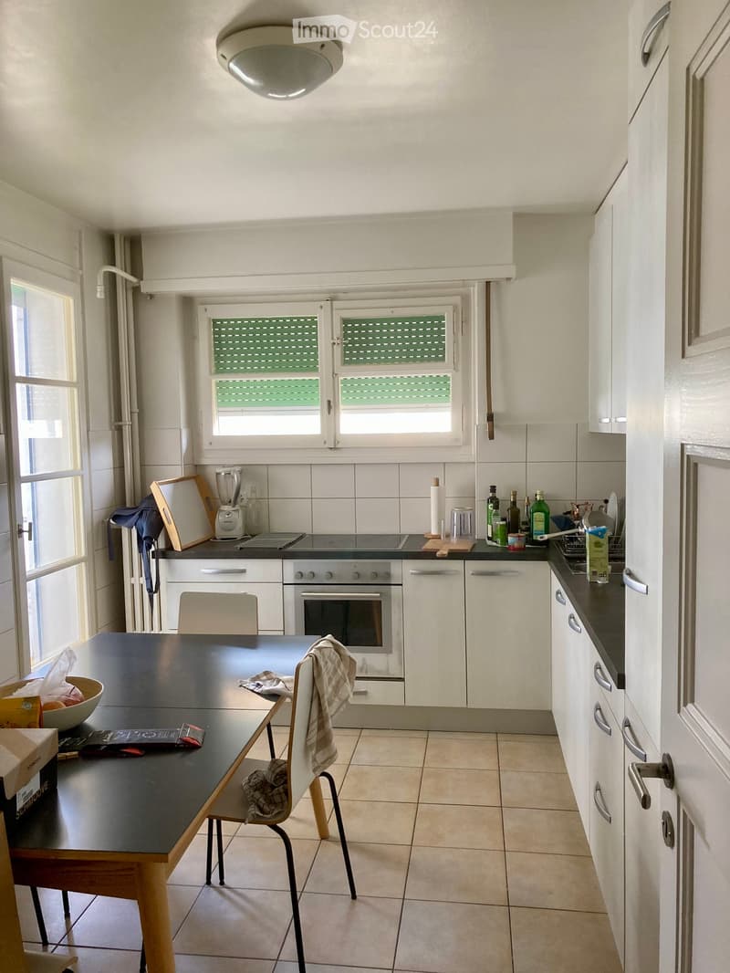 Modern kitchen with white cabinets, black countertops, and a central island table. Appliances include an oven, blender, and various kitchen items on the counters.
