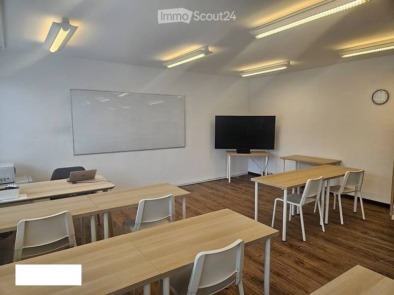 Classroom with wooden tables, white chairs, a laptop, a large screen, and a whiteboard.