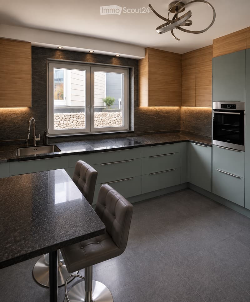 Modern kitchen with grey cabinets, dark countertops, stainless steel sink, built-in oven, and two leather stools at a central island.