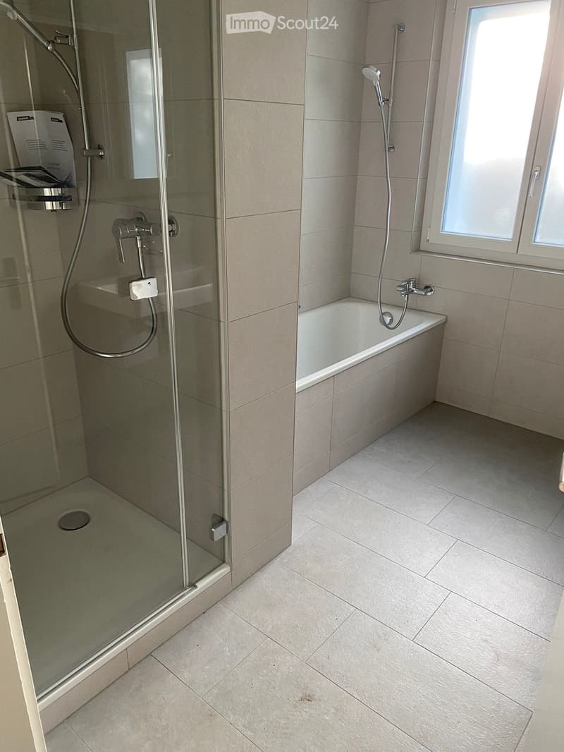Modern bathroom with a bathtub, glass-enclosed shower, and tiled walls and floor.