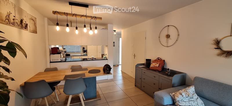 Open-plan living and dining area with a modern sofa, coffee table, dining table with chairs, and a fully equipped kitchen area with cabinets, appliances, and a sink.