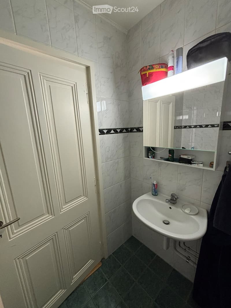 A small bathroom with marble tiles, a white sink, a mirror with a built-in cabinet, and a toothbrush on the sink counter.