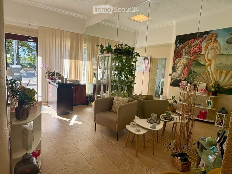 Well-lit room with a beige sofa, coffee table, side tables, decorative plants, a large mirror, and a cabinet. The space features a mix of modern and classic decor, including artwork and a vase on a side table.