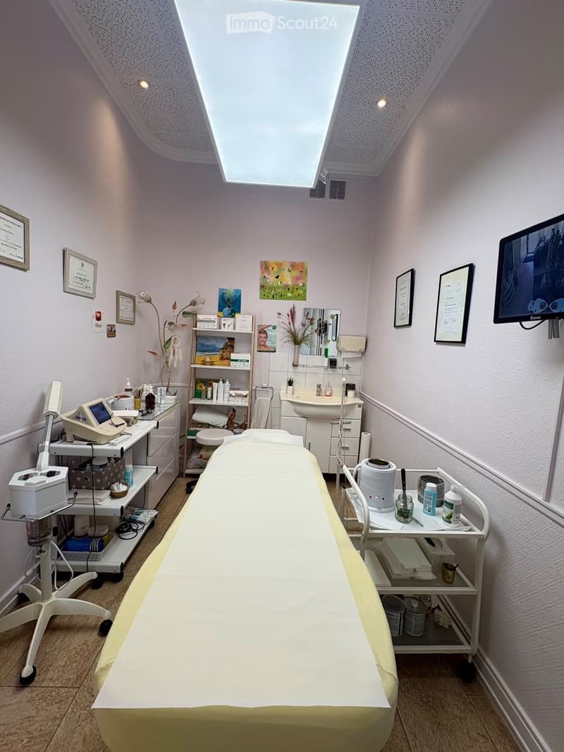 A well-lit, clean, and organized treatment room with a large treatment table, a sink, shelves with supplies, a mirror, a screen, and decorative elements.