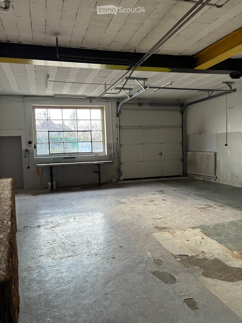 Empty room with a large window, a table, a white bucket, a radiator, and a garage door.