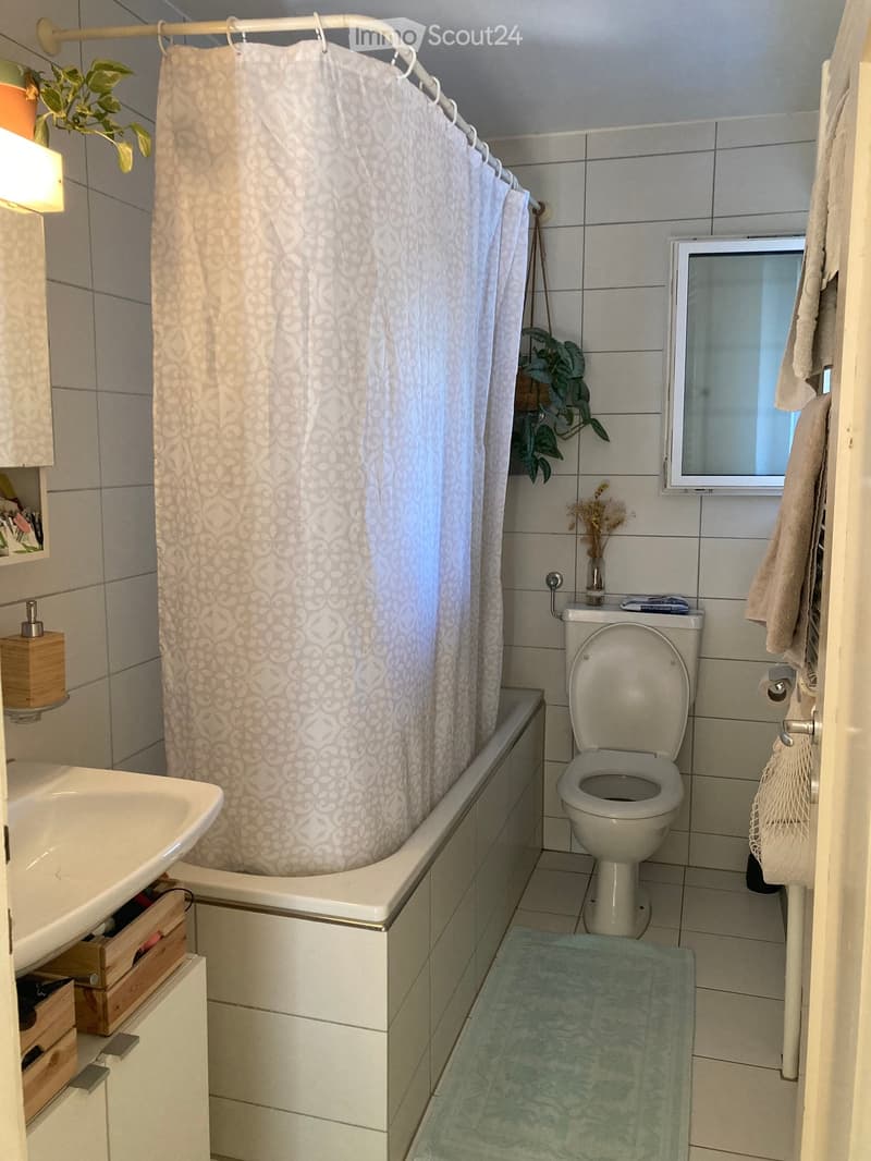 Bathroom with a bathtub, toilet, sink, and a shower curtain. Includes a towel, a small plant, and a mirror above the sink.