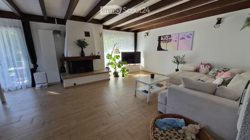 Living room with wooden flooring, exposed wooden beams, fireplace, sofa, coffee table, television, and decorative plants.
