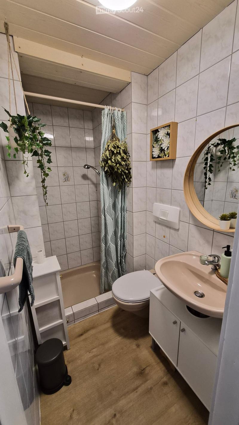 Modern bathroom with white tiles, wooden floor, toilet, sink, mirror, and a small shower area with a curtain.
