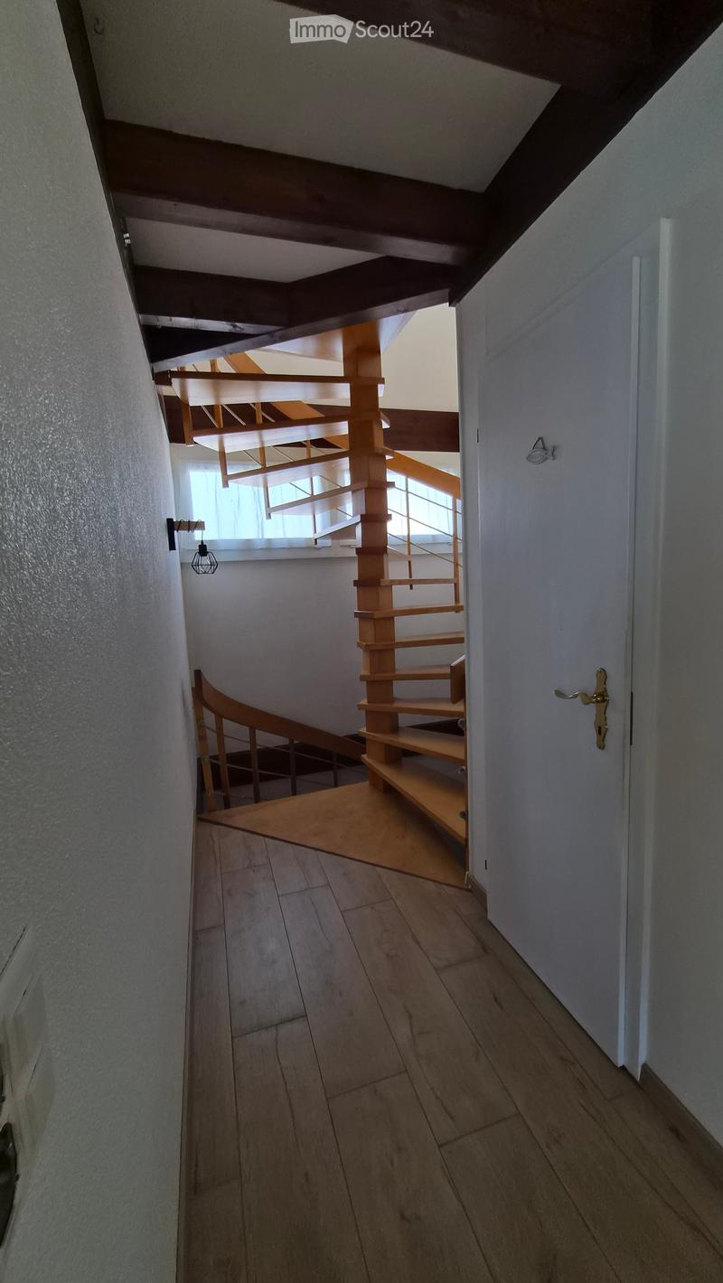 A modern hallway with wooden flooring, a staircase with wooden steps and railings, and a small window providing natural light.