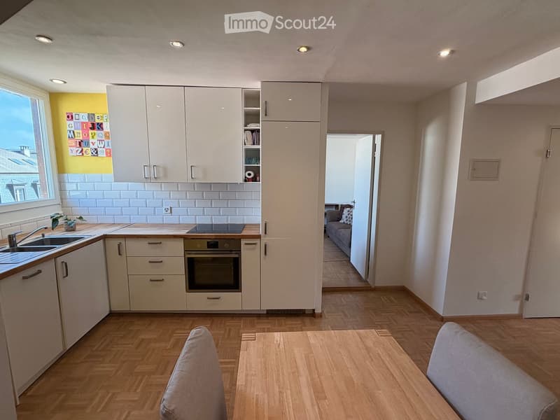 Modern kitchen with white cabinets, wooden countertops, and a sink, connected to a living area with a sofa and a small table.