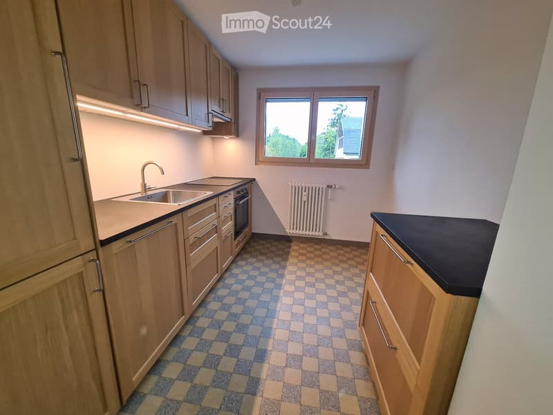 Modern kitchen with light wooden cabinets, stainless steel sink and faucet, built-in oven, and a checkered tile floor.