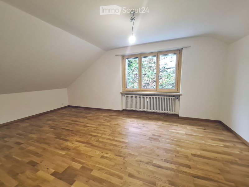 Empty room with wooden flooring, white walls, and a large window with a radiator below it.