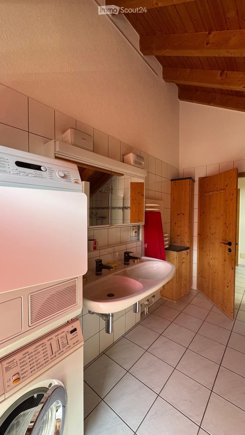 Bathroom with a double sink, washing machine, tiled walls and floor, and wooden cabinetry.