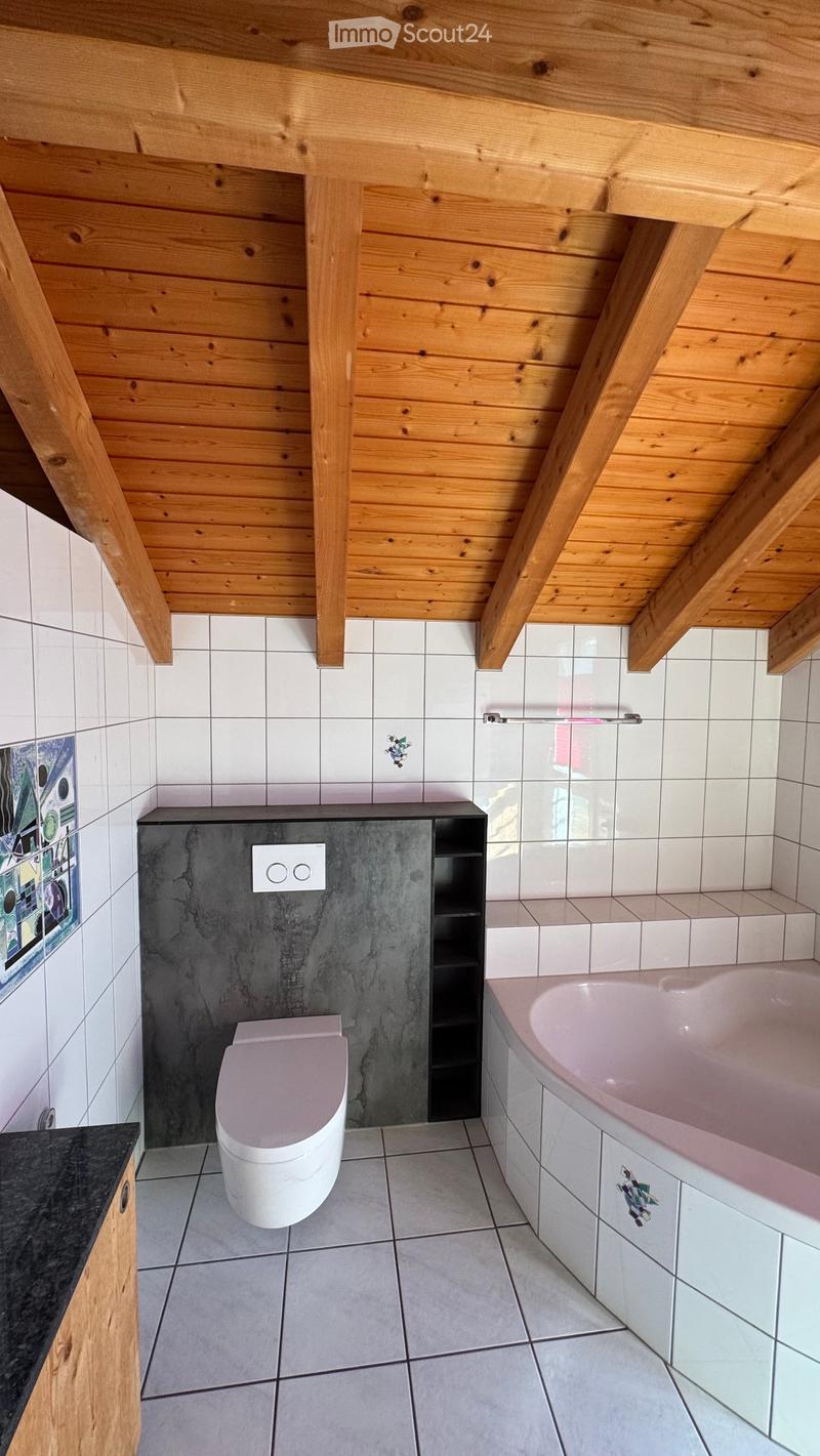 Modern bathroom with wooden ceiling beams, white tiled walls, a white toilet, a pink bathtub, and a dark grey cabinet with shelves.