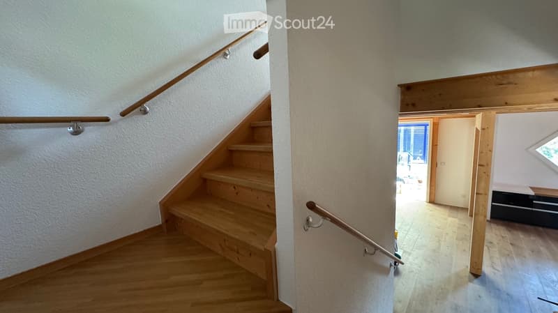Wooden staircase with metal handrail leading to an open area with wooden flooring and white walls.