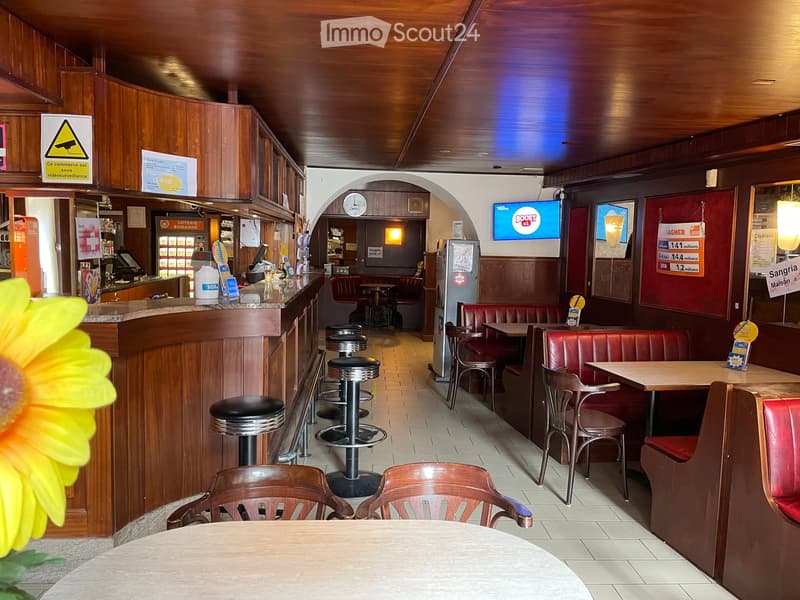 Restaurant interior with wooden walls and ceiling, featuring red leather booths, wooden tables, and bar stools.