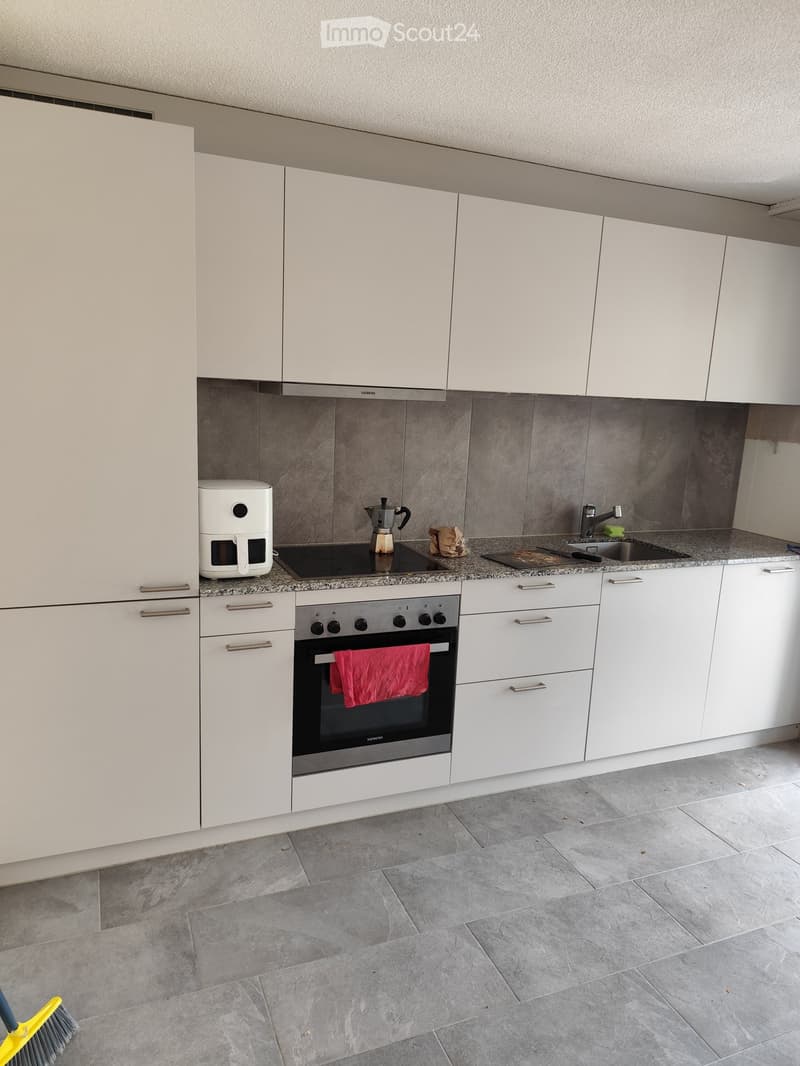 Modern kitchen with white cabinets, granite countertops, and stainless steel appliances including an oven, coffee maker, and induction stove. A red towel hangs from the oven door.