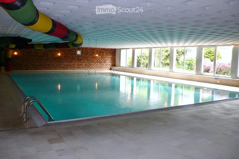 Indoor swimming pool area with large windows, tiled walls, and a decorative ceiling with a colorful pipe design.