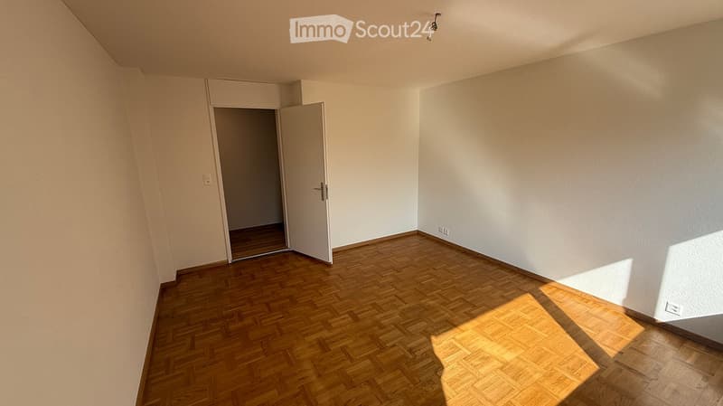 Empty room with wooden flooring, white walls, and a partially open door leading to another space.