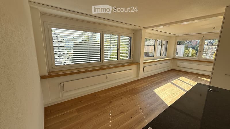 Empty room with wooden flooring, large windows with blinds, and radiators beneath the windows.