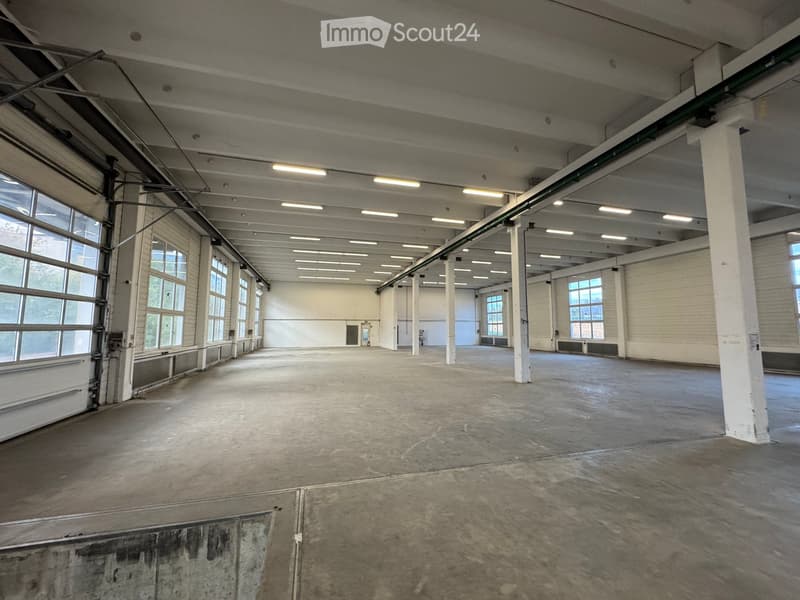 Large, empty industrial-style room with concrete floors, white brick walls, exposed steel beams, and large windows allowing natural light.