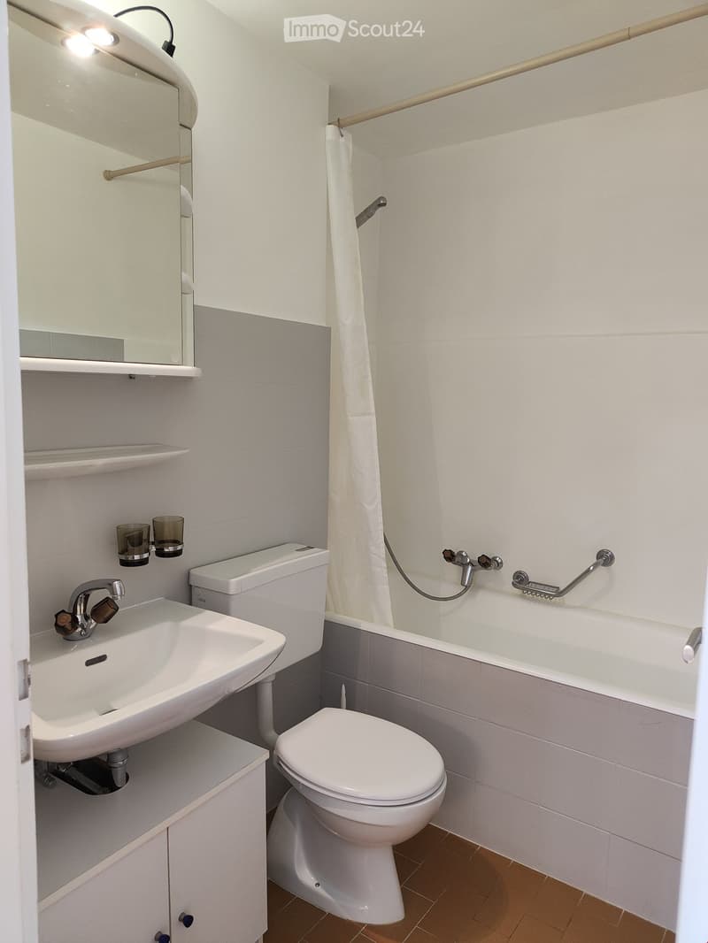 Modern bathroom with white tiles, a sink, toilet, bathtub, and a mirror above the sink. Includes a towel rack and two cups on the wall.