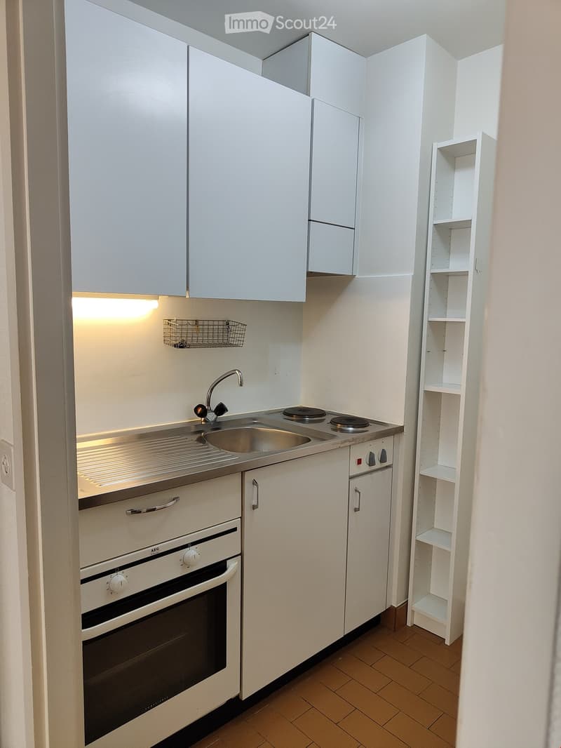 Compact kitchen with white cabinets, a sink, induction cooktop, oven, and a small shelf unit.