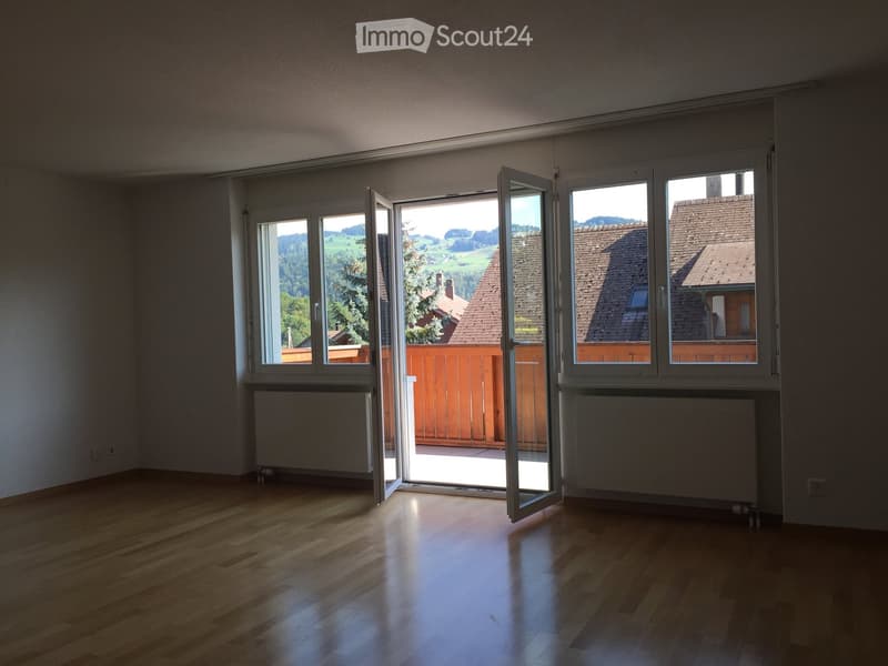 Empty room with wooden flooring, large windows, and radiators, offering a scenic view of the countryside through open sliding doors.