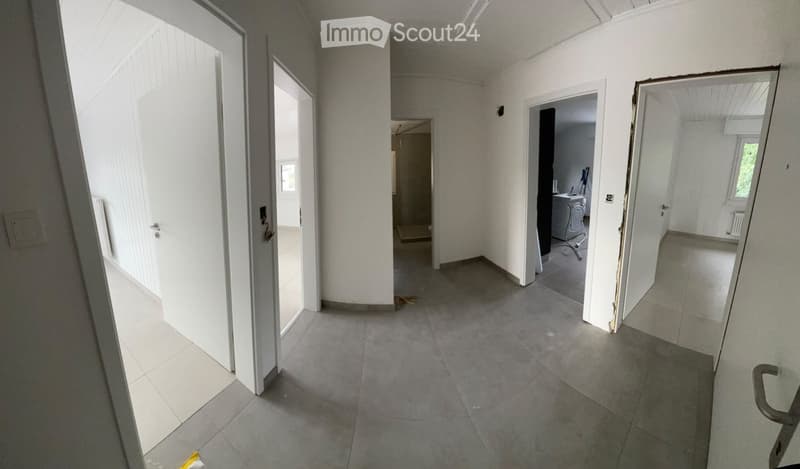 Empty hallway with white walls, grey tiled floor, multiple doors leading to different rooms, and a small area with a washing machine visible in the background.