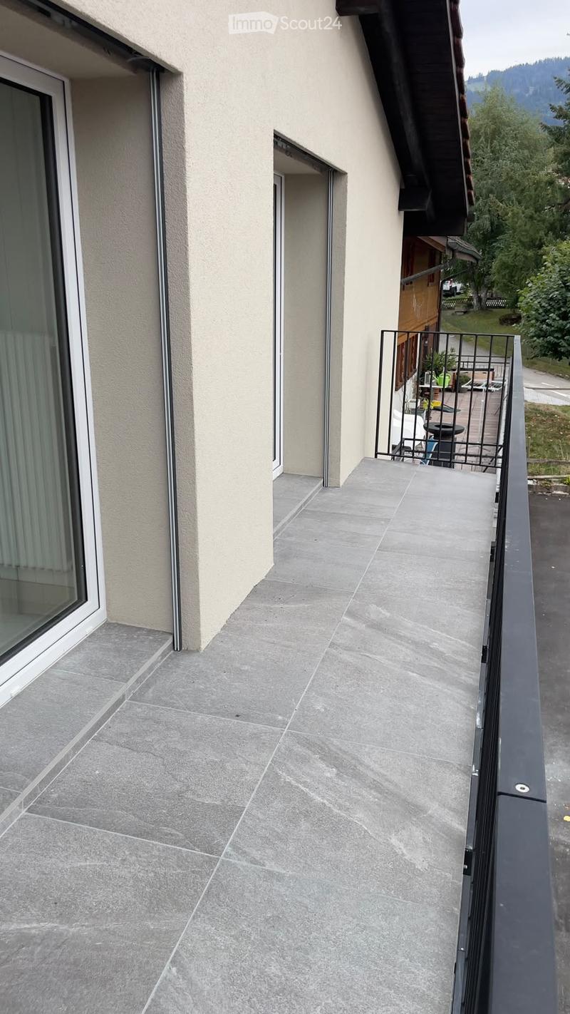 Balcony with grey tiled floor, metal railing, and a view of the surrounding greenery and a wooden shed.