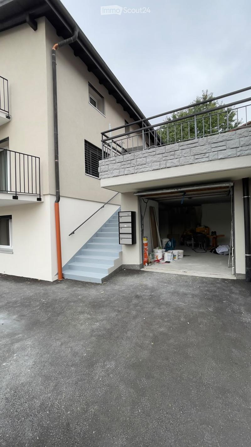 Two-story building with beige walls, multiple windows, balconies, and an open garage with construction materials inside.