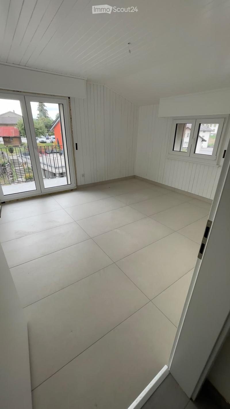 Empty room with white walls, tiled floor, and large windows, including a sliding glass door leading to an outdoor area.