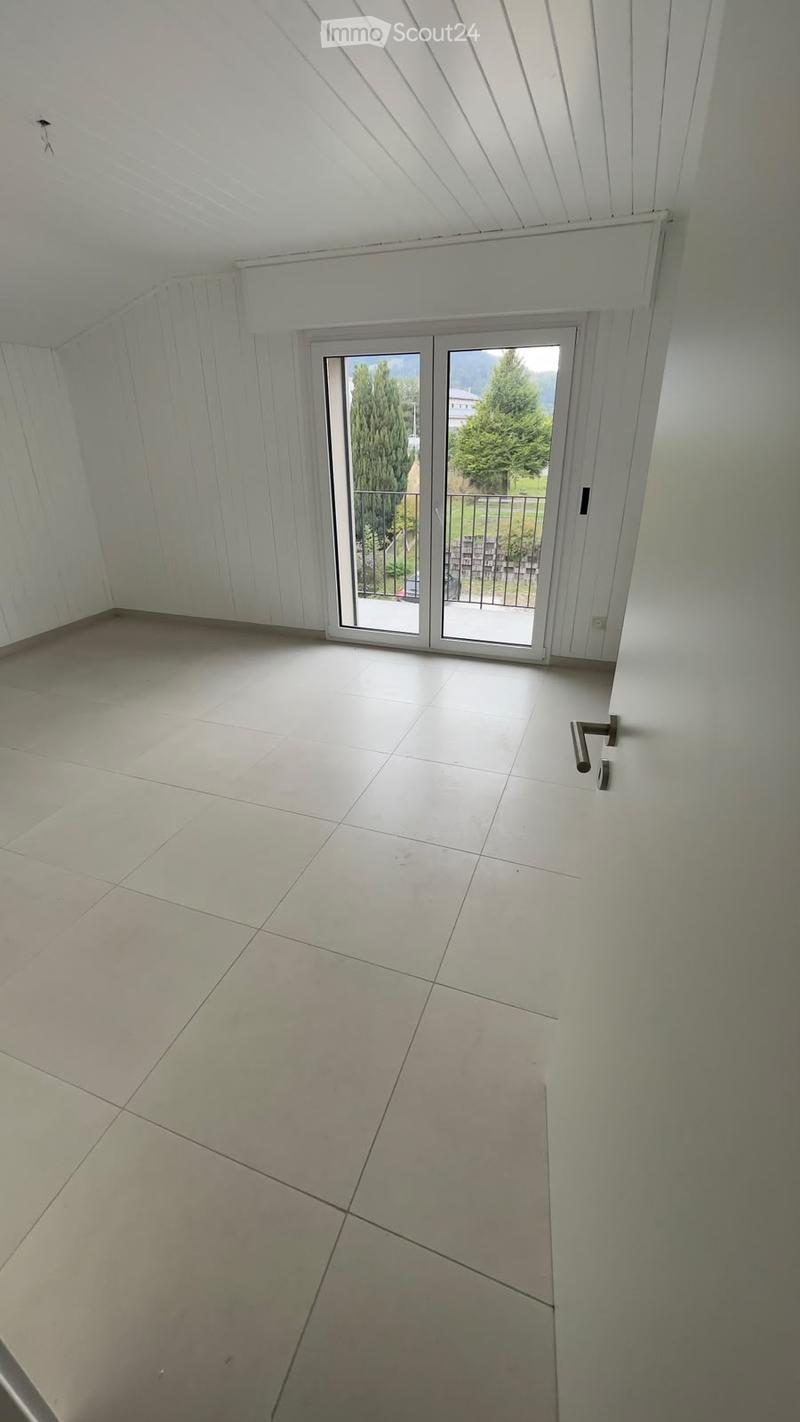 Empty room with white walls, tiled floor, and large sliding glass door leading to a balcony with outdoor view.