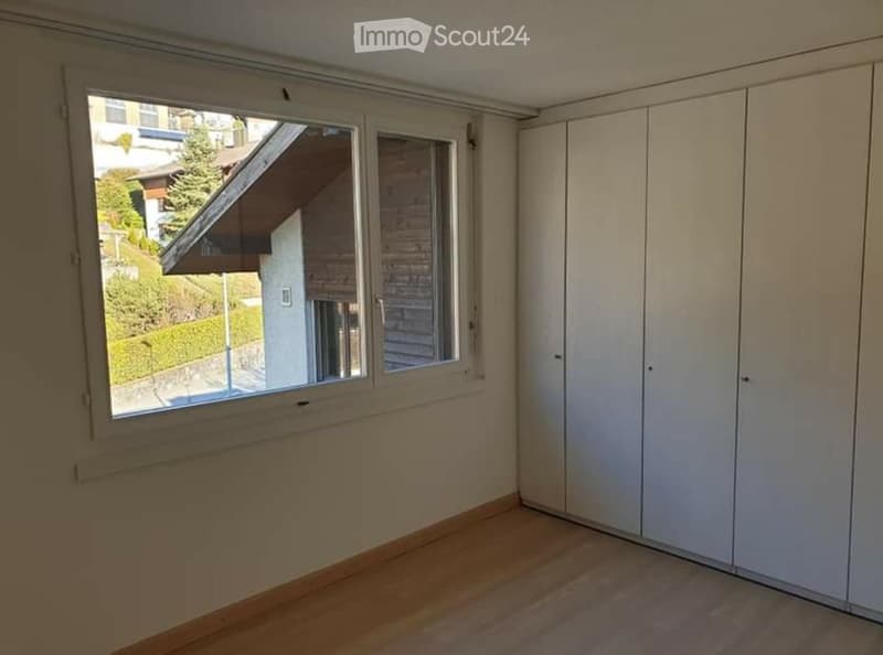 Empty room with wooden flooring, white built-in wardrobes, and large windows offering a view of the outside area.