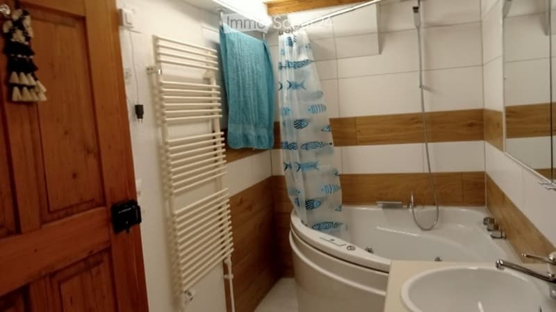 Cozy bathroom with a bathtub, sink, towel rack, and blue towels. The walls are tiled with a wooden trim design.