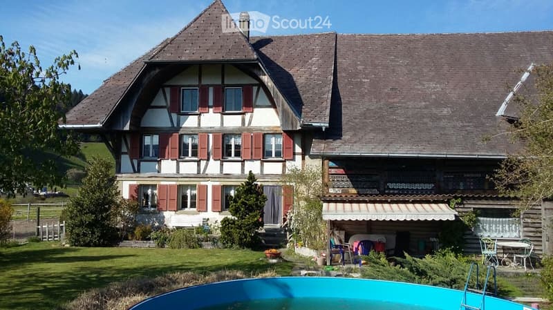 Two-story house with red shutters and a tiled roof, surrounded by a well-maintained garden and a swimming pool.