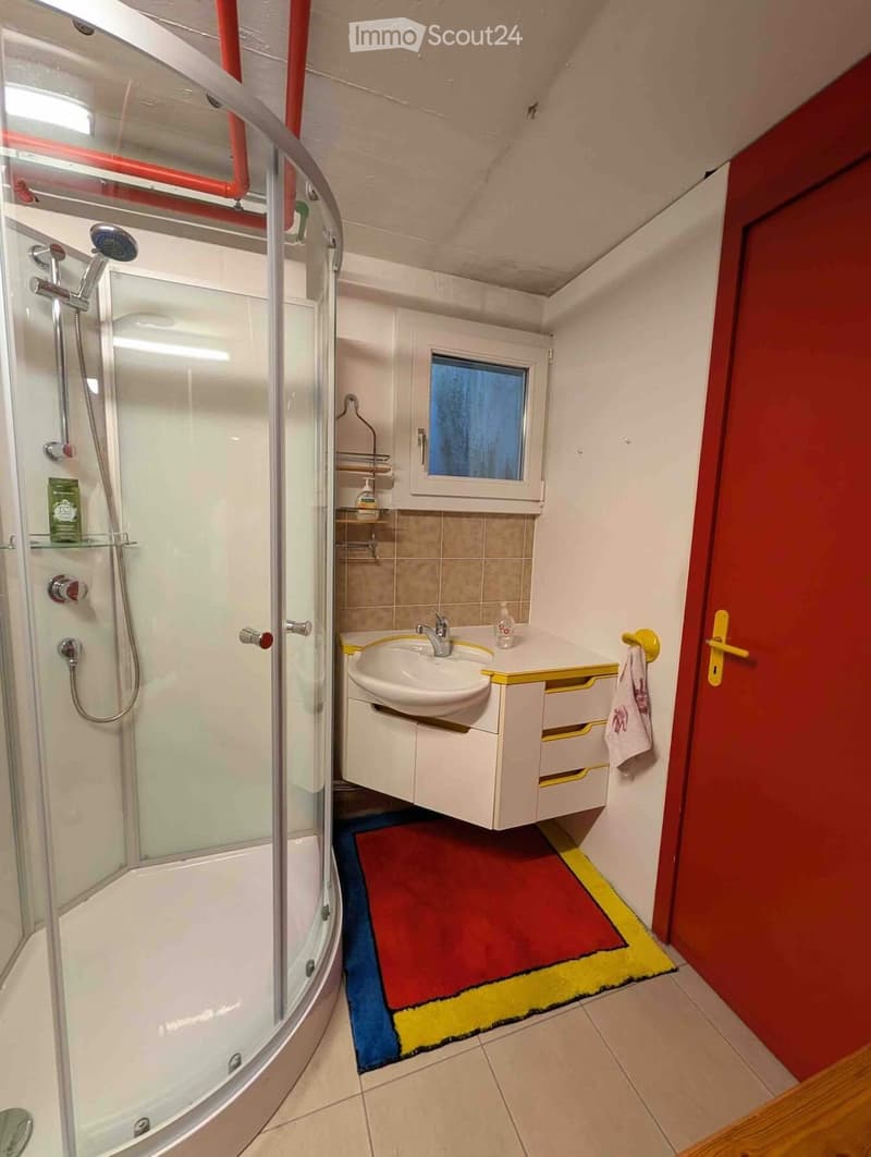 Modern bathroom with a glass-enclosed shower, a white sink with a yellow cabinet, a towel hanging on a rack, and a small window above the sink.