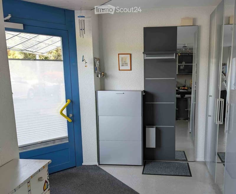 Hallway with a blue door, a small refrigerator, and a view into a kitchen area with a table and chairs.