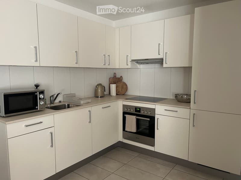 Modern kitchen with white cabinets, stainless steel appliances, and a tiled backsplash. Includes a microwave, oven, sink, and countertop items.