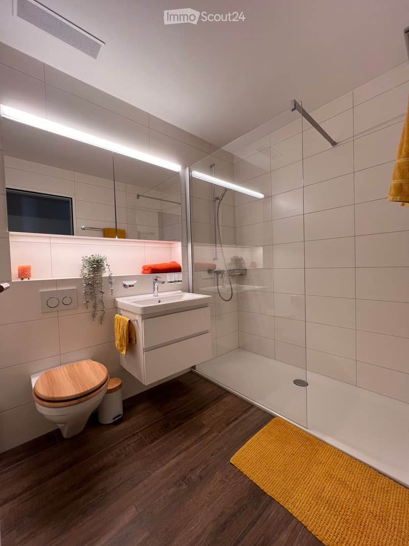 modern bathroom with toilet, sink, shower, and tiled walls